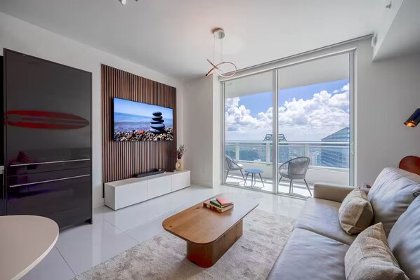 Ein modernes Wohnzimmer mit Flachbildfernseher, einer Holz-Unterhaltungsecke, einer Couch, einem Couchtisch und einem Balkon mit Blick auf die Stadt.