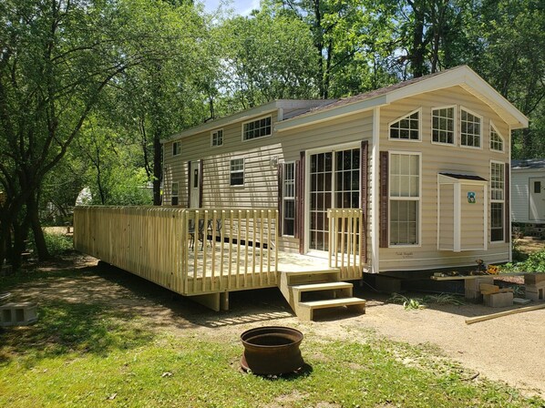 A small, single-story cabin with a deck and a front porch, surrounded by trees.