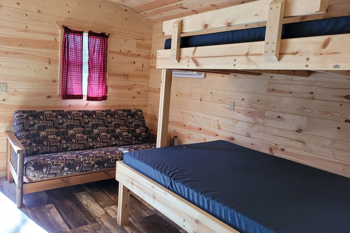 Une chambre de chalet en bois avec un lit superposé, un canapé à motifs et une fenêtre avec des rideaux rouges.