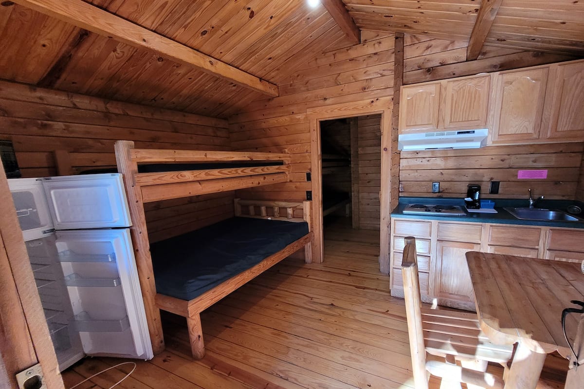 Une cabane en bois avec des lits superposés, un coin cuisine et un espace repas.