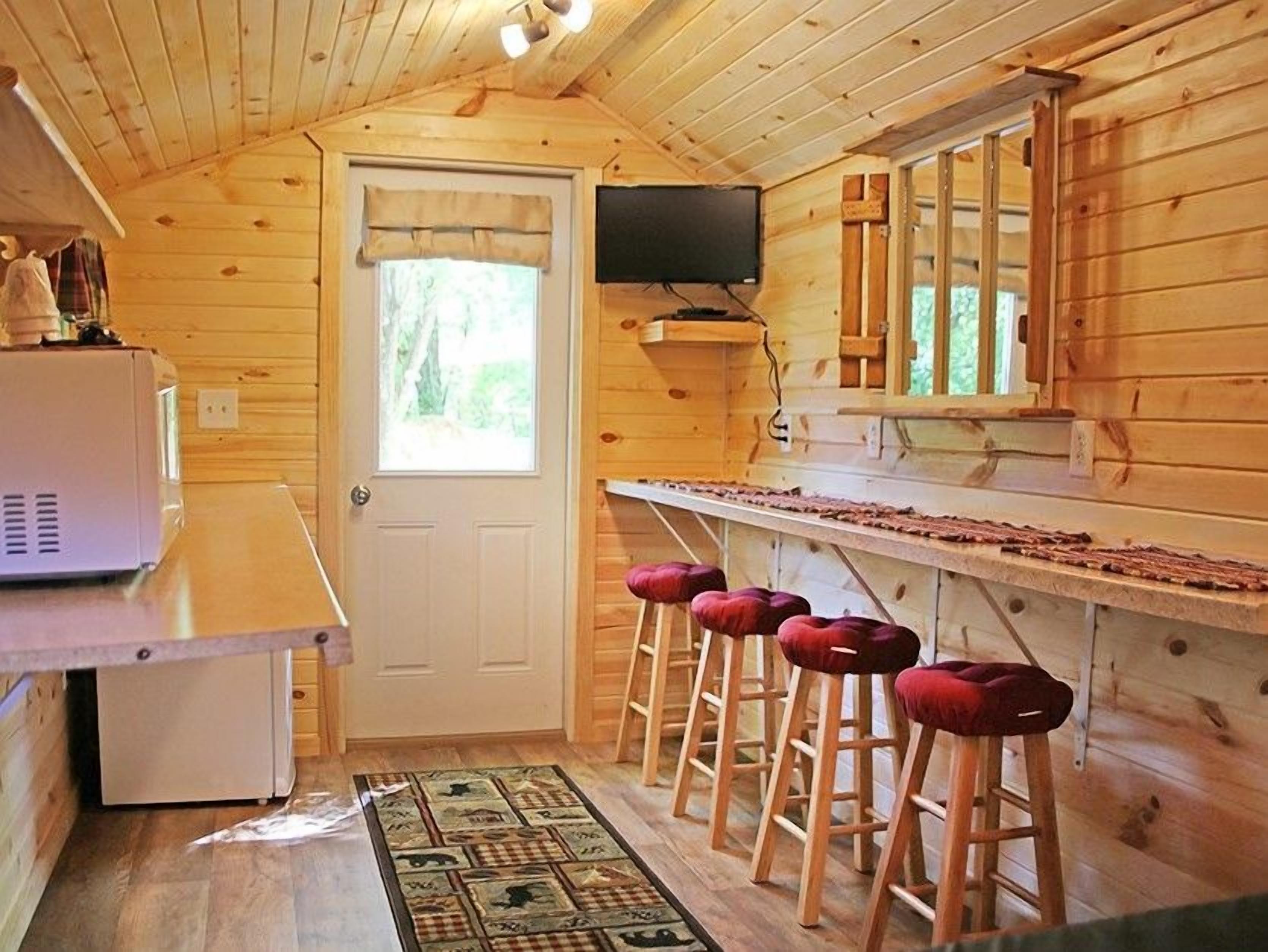 Una cocina compacta con refrigerador, microondas y mostrador de madera con taburetes.