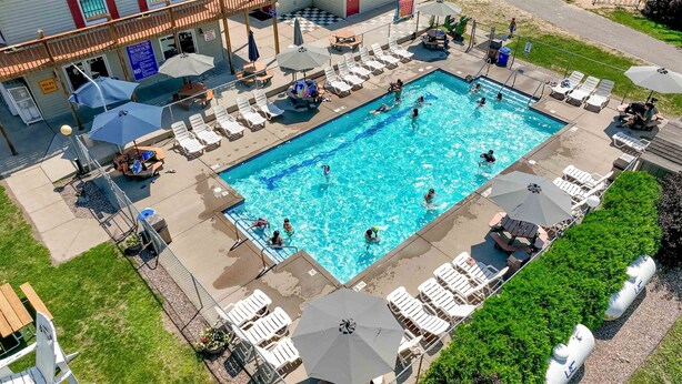 A swimming pool with lounge chairs and umbrellas, surrounded by a fence and greenery. - Baraboo RV Resort (Baraboo)