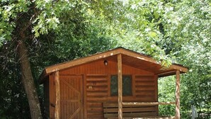 A wooden cabin with a porch, a bench, and a picnic table. - Baraboo RV Resort (Baraboo)