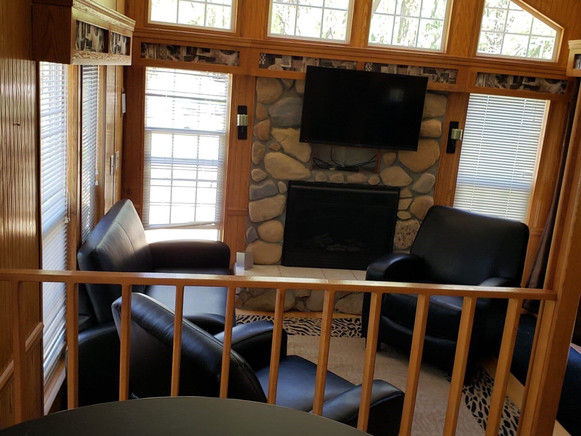 A cozy living room with a stone fireplace, a flat-screen TV mounted above it, and leather seating.