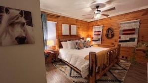 A cozy wooden room with a bed, a ceiling fan, and a rug. - Natural State Cabins - 5 Cabin Listing (Hot Springs)