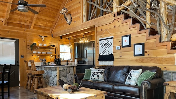 A rustic cabin interior with a stone fireplace, wooden furniture, and a stone wall. - Natural State Cabins - 5 Cabin Listing (Hot Springs)