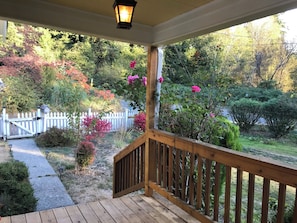 Eine Holzterrasse mit Geländer, ein weißer Zäune und ein Garten mit verschiedenen Pflanzen und Blumen.
