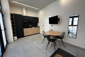 A modern kitchen with black cabinets, a wooden dining table, and a TV mounted on the wall. - Travel Habitat Jardin Ayora 2 WIFI+AACC (Valencia)