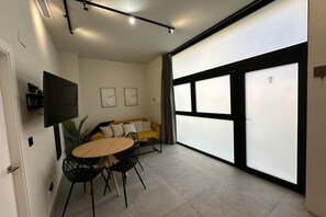 A modern living space with a dining area, a sofa, and a large window. - Travel Habitat Jardin Ayora 2 WIFI+AACC (Valencia)