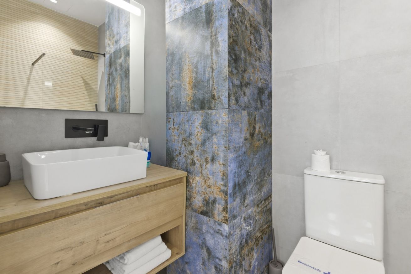 A modern bathroom with a wooden vanity, a white bathtub, and a toilet with a 'Desinfectado' label.