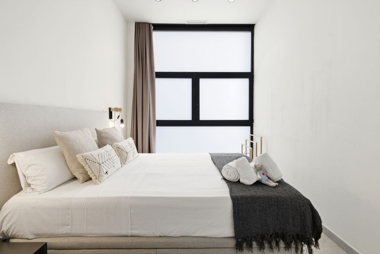 A bedroom with a large bed, a window with curtains, and a bedside table with a lamp.