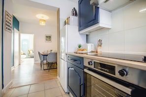 A modern kitchen with a built-in oven, a microwave, and a dining area with a table and chairs. - Elegant City Retreat | Free Parking | 13 PPL (Sheffield)