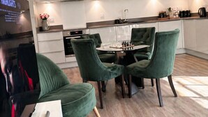 A modern kitchen with white cabinets, a round dining table with green upholstered chairs, and a TV mounted on the wall. - Stylish 2-Bed Apt 
| 10 Mins to Oxford Universities/city | Free private parking (Oxford)