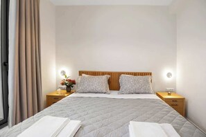 A neatly arranged hotel room with a bed, two bedside tables, a nightstand, and a window with curtains. - Mitos Luxury Villas Gerani/Heated Pool*/Sleeps20 (Pirgos Psilonerou)