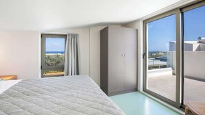 Een hotelkamer met een bed, een kledingkast, een schuifdeur naar een balkon en een raam met uitzicht op de stad.