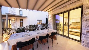 Een terras met een tafel voor vier personen, omgeven door stenen muren en een glazen deur die naar een kamer leidt.