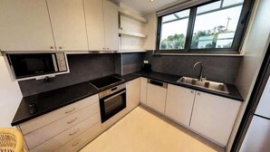 Een kleine keuken met een magnetron, oven, spoelbak en kastjes.