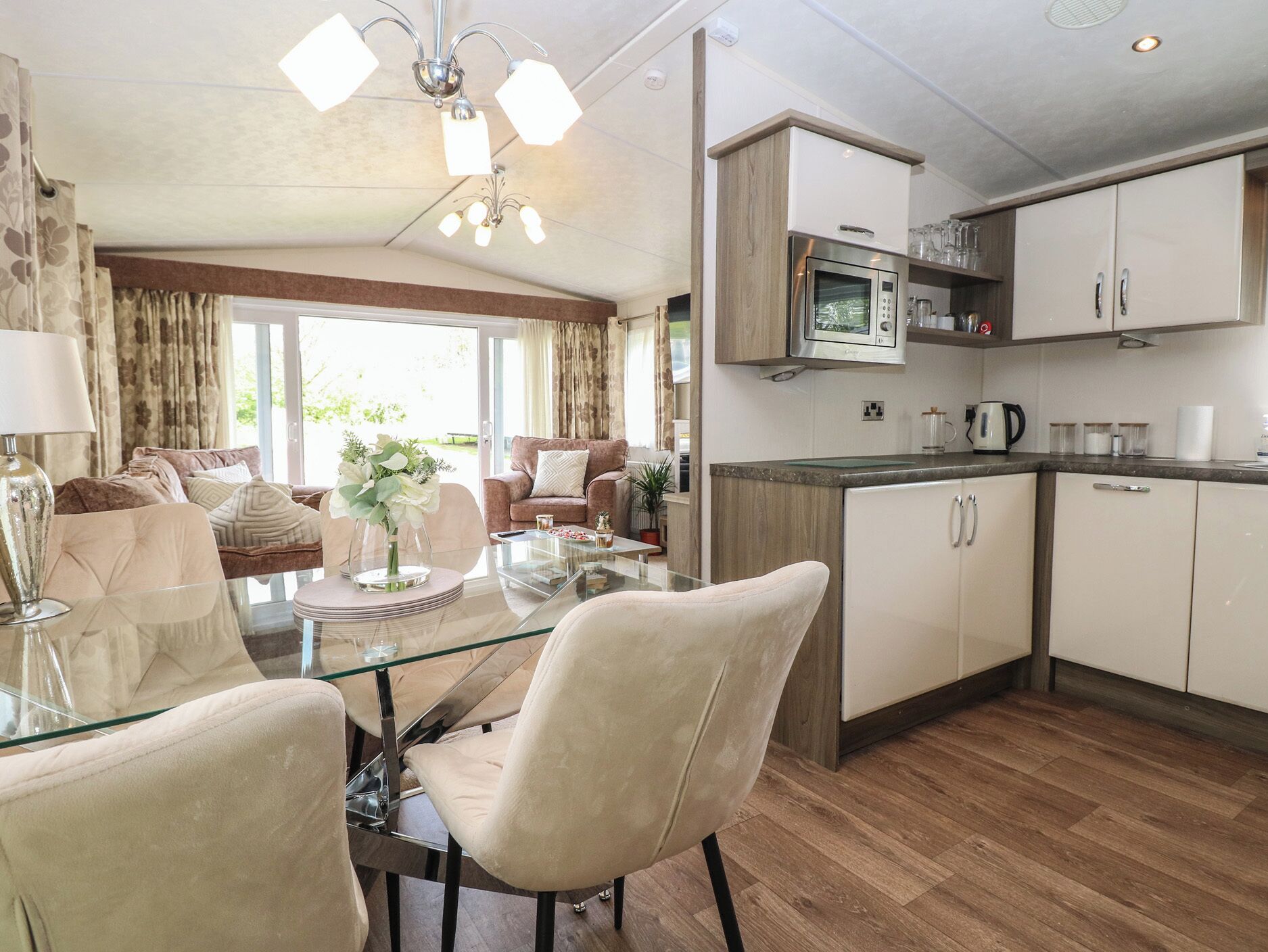 A modern kitchen with a microwave, cabinets, and a coffee maker. There is a dining area with a glass table and chairs.