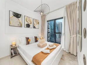 A modern bedroom with a large bed, artwork on the wall, a nightstand, and a view of the city. - Skyline View High-Floor Apartment mit Pool (Dubai)