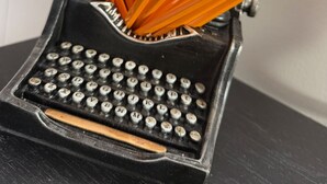 Een oude typemachine met een potloodhouder met daarin verschillende potloden.