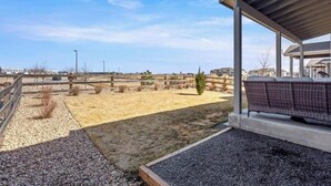 En overdækket terrasse med siddeplads, en grussti og en indhegnet udendørs område.