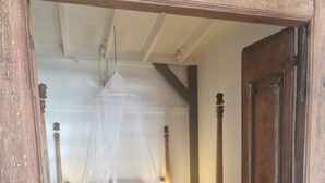Un dormitorio con cama a dosel, banca de madera, alfombra redonda y puerta de madera.