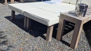 Una cama con colchón blanco, estructura de madera y una mesita con una cámara y una botella.