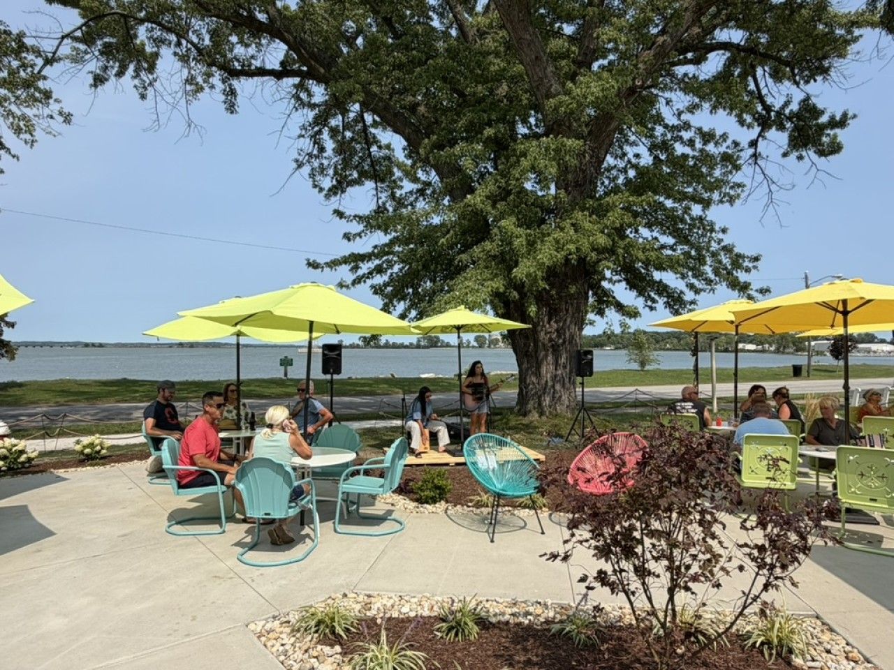 An outdoor seating area with tables and chairs under yellow umbrellas, overlooking a body of water.