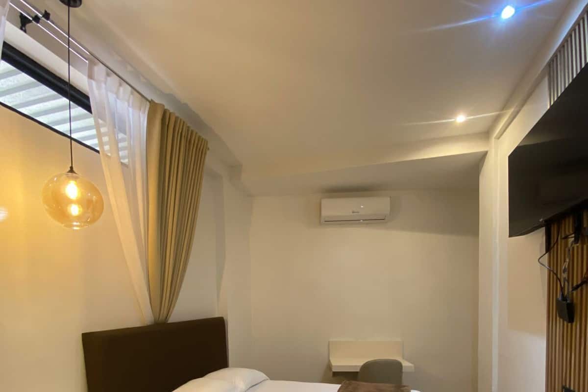 A hotel room with two beds, a desk, an air conditioning unit, and a television.
