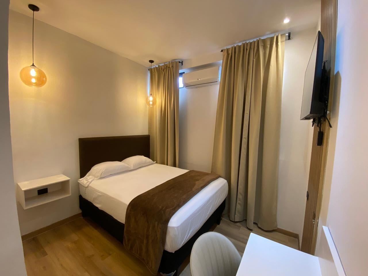 Een hotelkamer met een bed, nachtkastje, televisie en gordijnen.