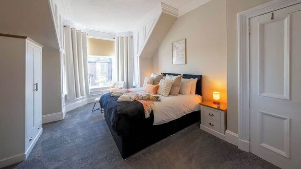 A bedroom with a bed, bedside table, and a window. - Balmoor House - 4 Beds in Peterhead near the coast (Aberdeenshire)