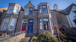 A stone building with a red door, multiple windows, and a small garden area. - Balmoor House - 4 Beds in Peterhead near the coast (Aberdeenshire)
