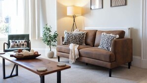 A living room with a brown sofa, a lamp, a framed picture, and a small table with a bowl. - Balmoor House - 4 Beds in Peterhead near the coast (Aberdeenshire)