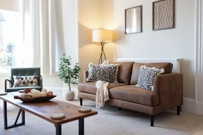 Ein Wohnzimmer mit braunem Sofa, einer Lampe, einem gerahmten Bild und einem kleinen Tisch mit einer Schale.