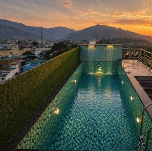 Una piscina a sfioro sul tetto con una cascata, circondata da una città e montagne.