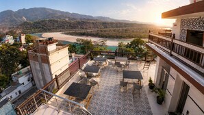 A terrace with outdoor seating, a view of a river, and mountains in the background.