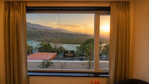 A hotel room with a large window offering a view of a mountainous landscape, a road, and a sign for 'The Montara - A boutique hotel.' - Hotel Montarara Rishikesh (Rishikesh)