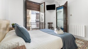 A bedroom with a bed, a TV, a bathroom, and a balcony.