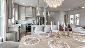A modern kitchen with white cabinets, a stainless steel refrigerator, and a dining area with a wooden table set with candles and woven placemats. - Private Pickleball Resort | Waterfront | Golf Cart (Carlton Landing)