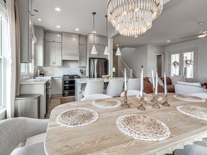 A modern kitchen with white cabinets, a stainless steel refrigerator, and a dining area with a wooden table set with candles and woven placemats. - Private Pickleball Resort | Waterfront | Golf Cart (Carlton Landing)