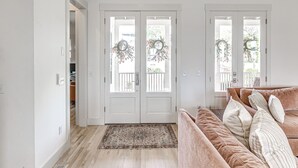 A room with a beige sofa, a patterned rug, and a double door with a wreath. - Private Pickleball Resort | Waterfront | Golf Cart (Carlton Landing)