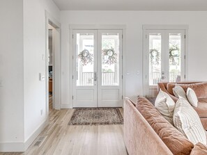 A room with a beige sofa, a patterned rug, and a double door with a wreath. - Private Pickleball Resort | Waterfront | Golf Cart (Carlton Landing)