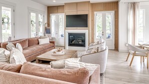 A spacious living room with a fireplace, a ceiling fan, and a large TV mounted above it. - Private Pickleball Resort | Waterfront | Golf Cart (Carlton Landing)