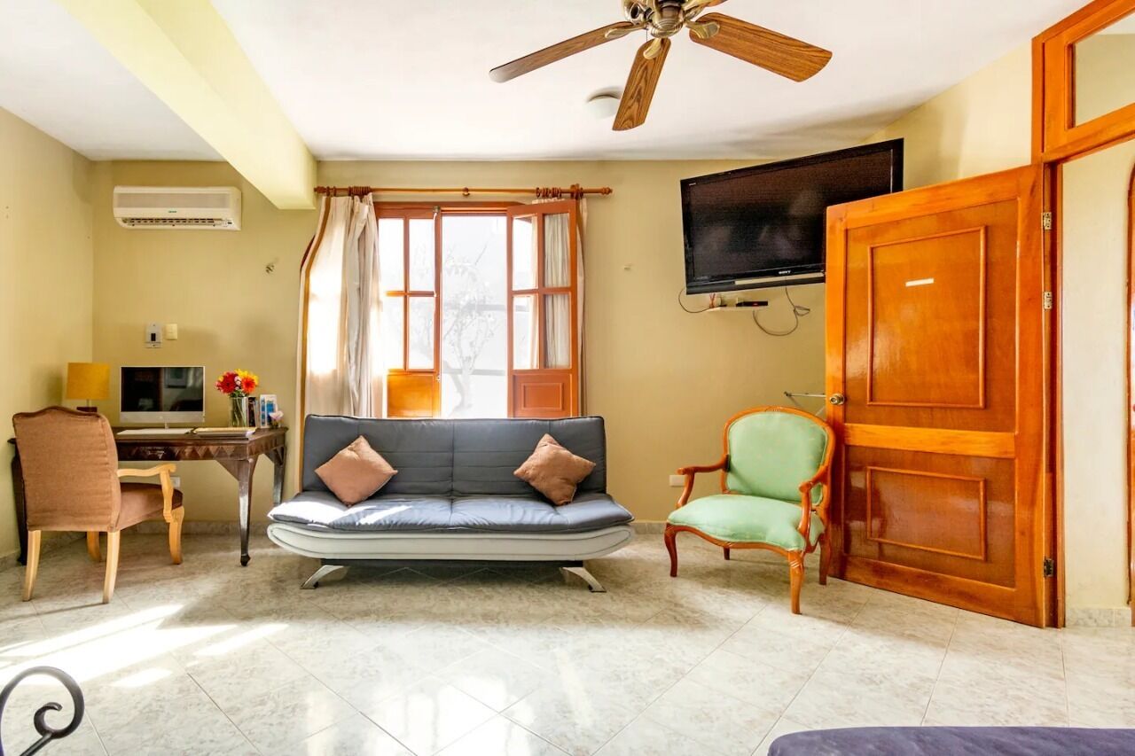 Una sala de estar con sofá, sillas, televisor, ventilador de techo y una puerta de madera.