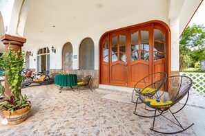 Ein überdachter Patio-Bereich mit Steinboden, einer Holztür und Sitzgelegenheiten im Freien.