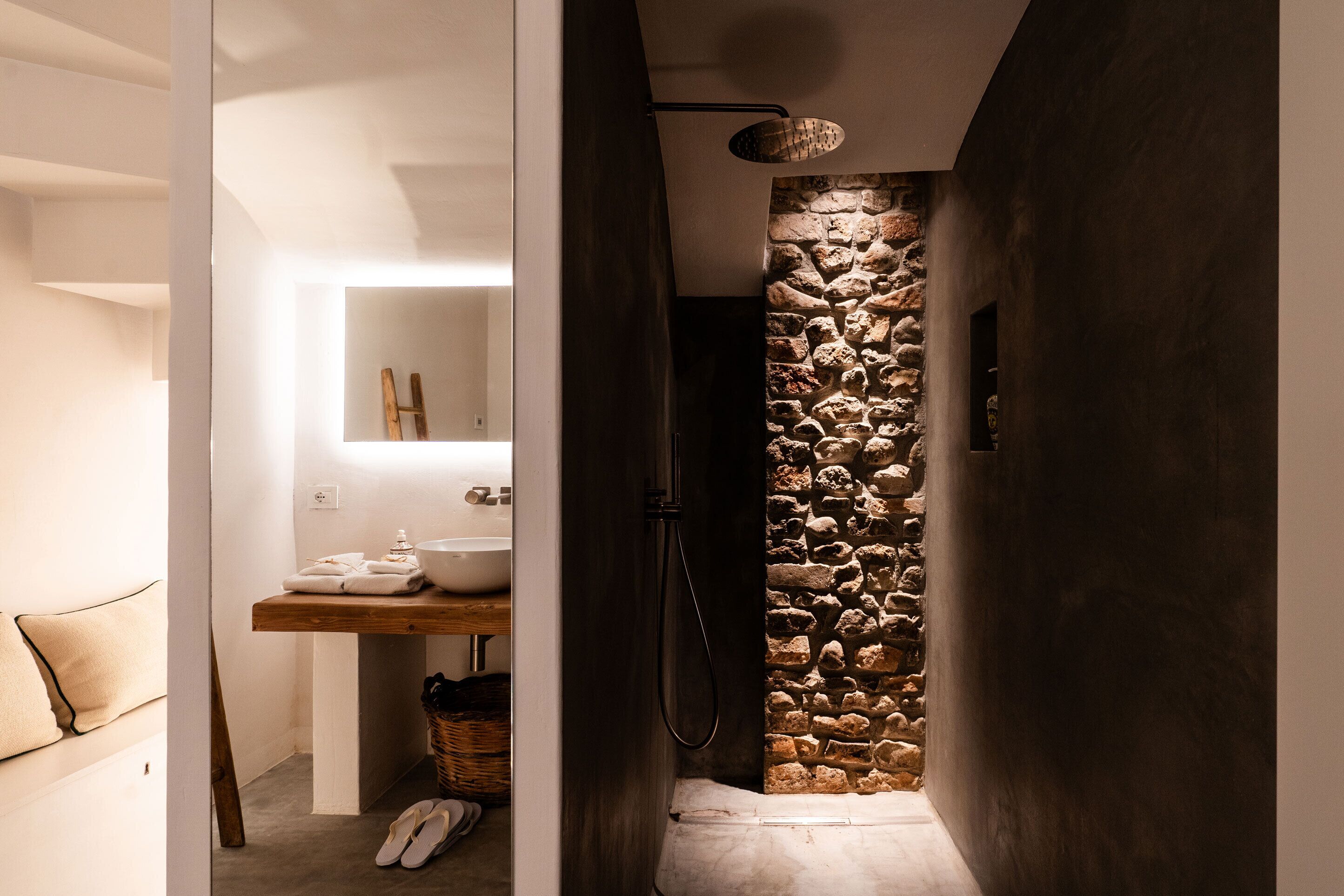 Ein modernes Badezimmer mit Wandverkleidung aus Stein, einem Holz-Waschtisch und einer Dusche mit einer außergewöhnlichen Leuchte.