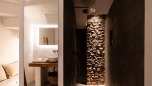 Et moderne badeværelse med en væg i natursten, et trækommode og en bruseniche med en markant lysarmatur.