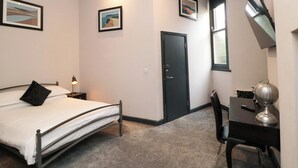 A bedroom with a bed, a desk, a chair, a door, and two framed pictures on the wall. - Craven Suite (Scarborough)