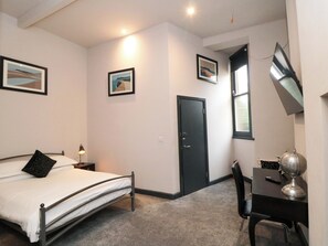 Un dormitorio con cama, escritorio, silla, puerta y dos cuadros en la pared.