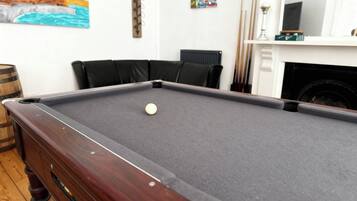 A pool table with a white cue ball, black cushions, and a wooden side table.